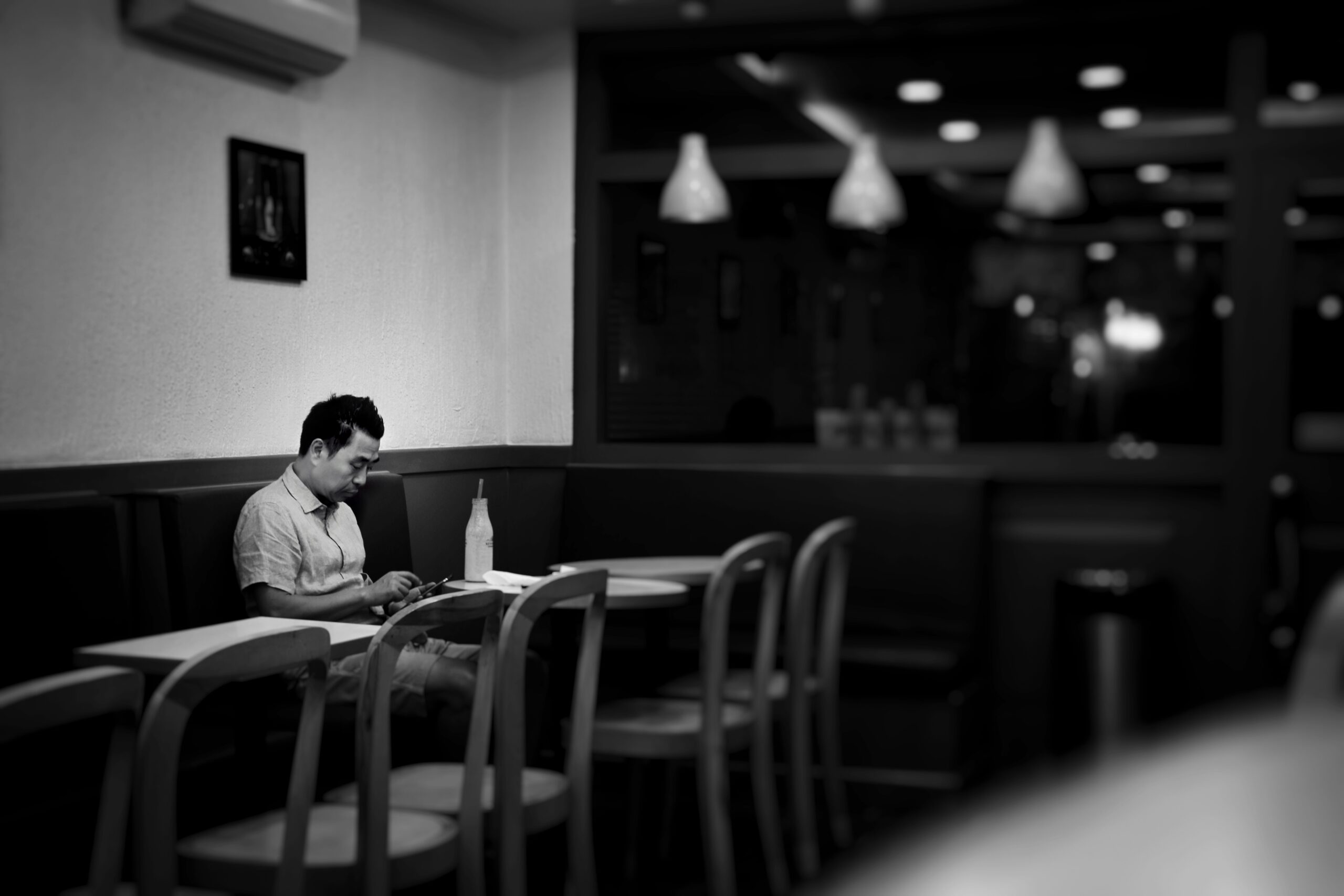 Man sitting alone in a café looking at his phone – highlighting social isolation, disconnection and the quiet struggle with loneliness many men face