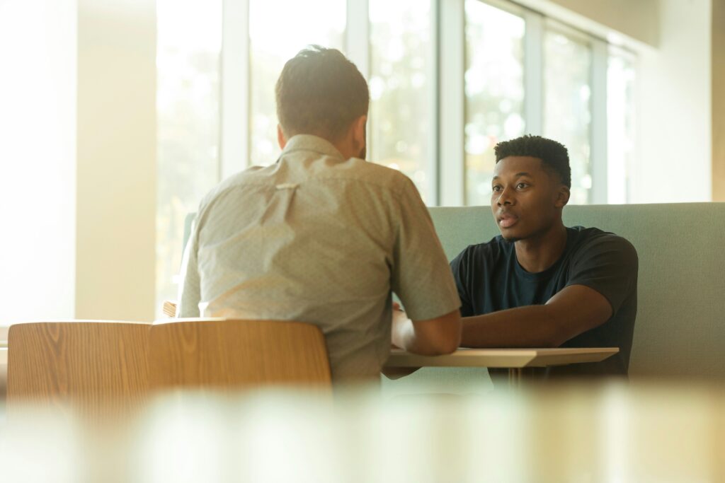 Two men talking at a café table with one actively listening – illustrating the importance of safe, supportive spaces for encouraging men to open up emotionally