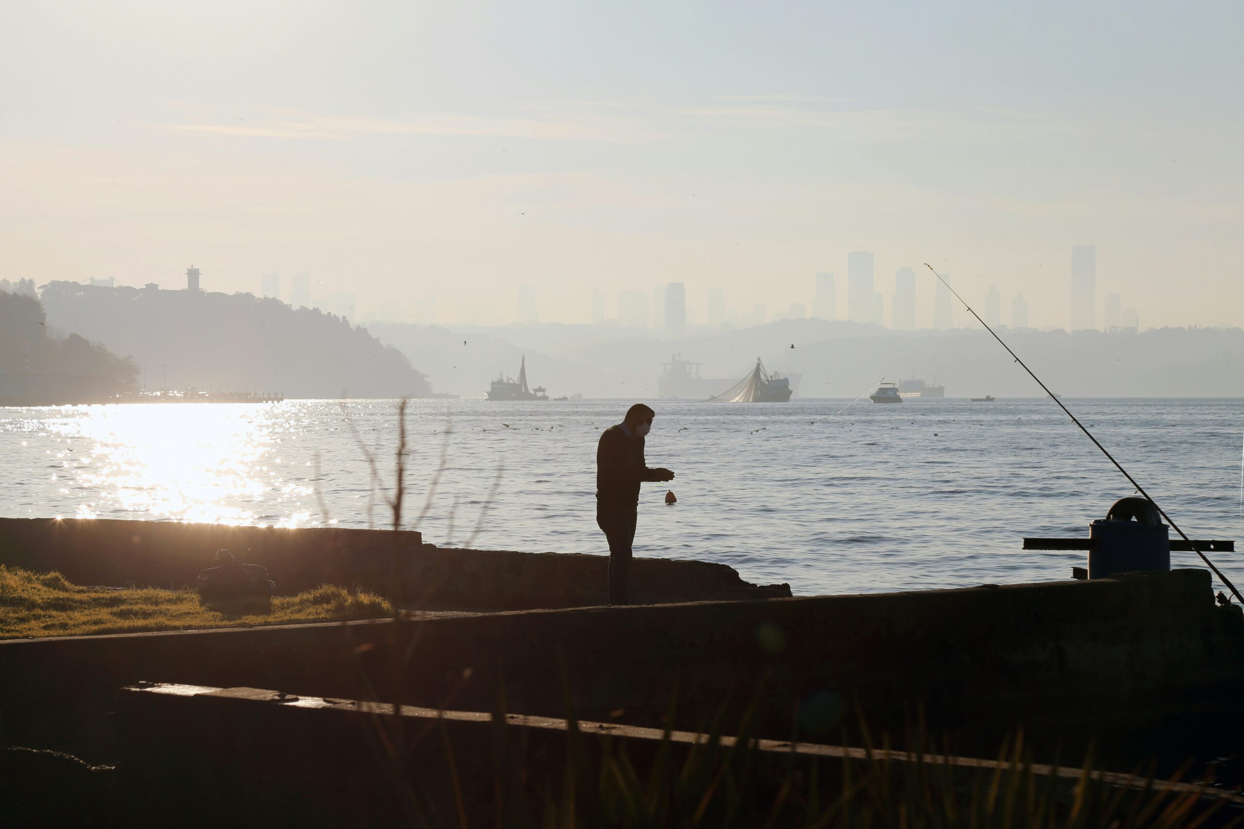 Older man standing alone by the water with fishing gear, silhouetted against a hazy skyline – representing loneliness and the search for connection in later life