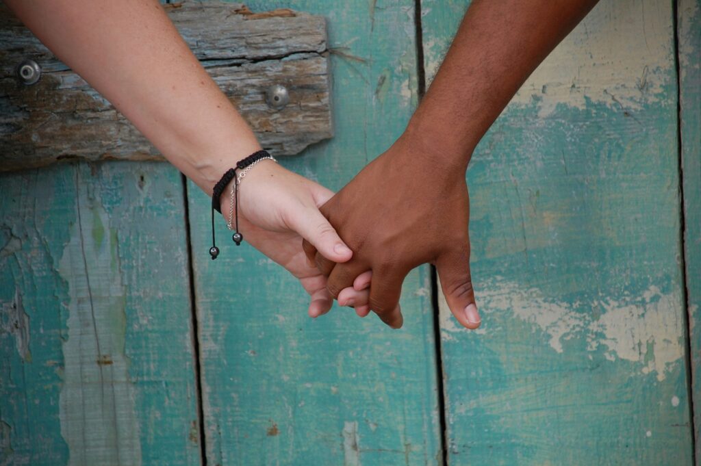 Close-up of two people holding hands against a rustic wooden background – symbolising trust, connection and emotional intimacy in men’s relationships