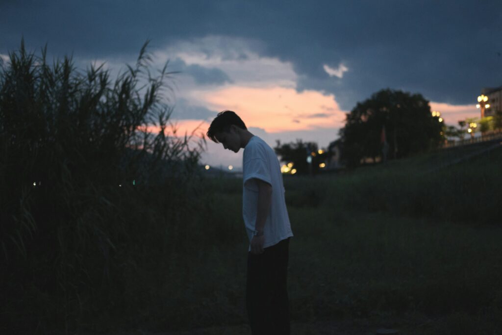 Young man standing alone at dusk, head bowed in quiet reflection – symbolising Stoic principles of inner stillness and emotional resilience